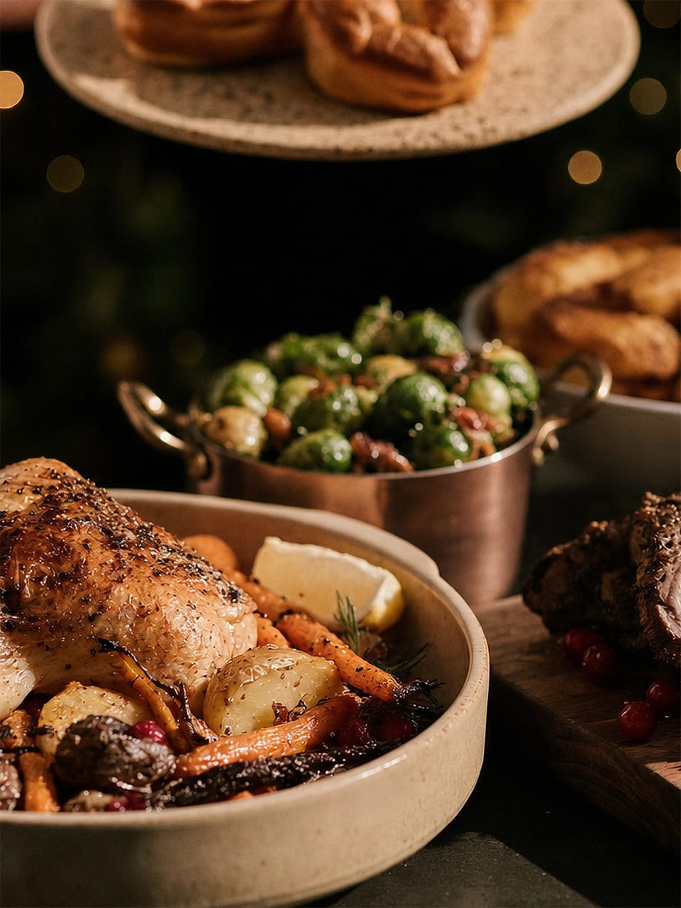 Festtagsbraten: gebratenes Geflügel mit Möhren und Kartoffeln in einer Keramikschale, dahinter Rosenkohl im Kupfertopf