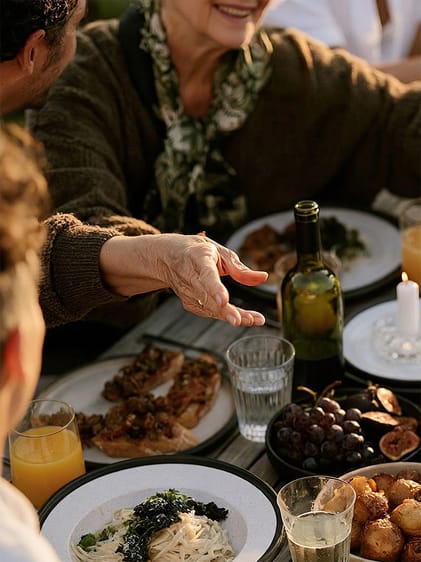 Hand greift über einen gedeckten Tisch mit Bruschetta, Pasta, Trauben und Wein