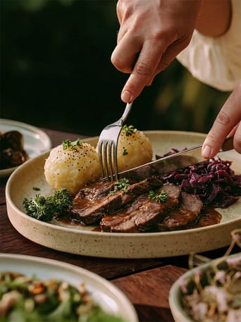 Gedeck mit geschmortem Fleisch, Kloß und Rotkohl, Besteck beim Anschneiden
